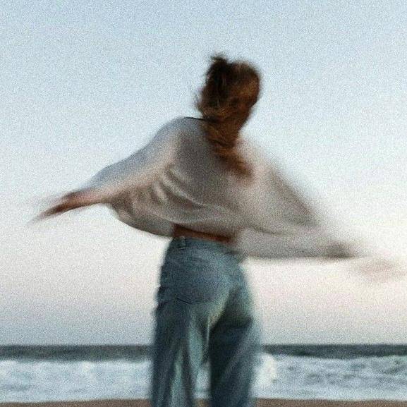 A woman in motion on the beach, arms open, blurred by movement