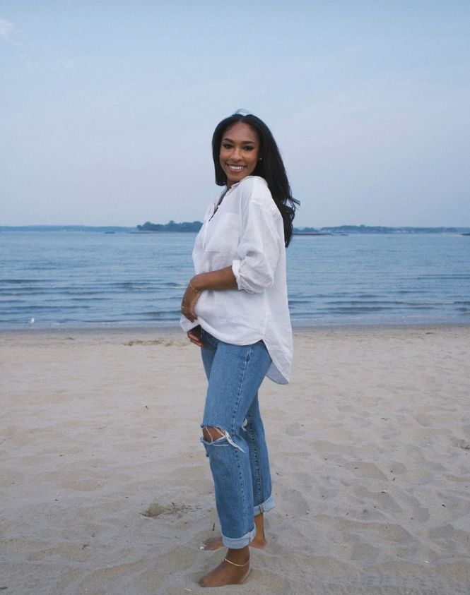 Jackie Shaw smiling on a beach at dusk, in a white linen shirt and rolled jeans