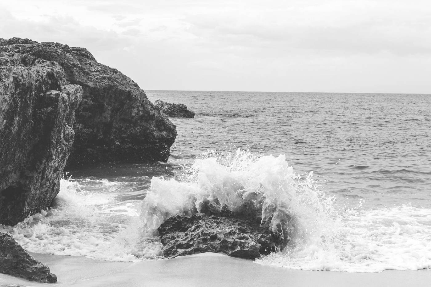 A wave breaking against dark rocks at the shoreline
